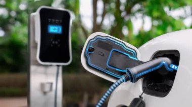 Doğal yeşil araba parkındaki ekolojik temiz enerji şarj istasyonundan gelen fütürist akıllı EV şarj aletinin şarj ettiği elektrikli araba. Alternatif enerji kullanan gelecekçi çevre dostu elektrikli araba. İnceleyin