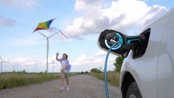 聚焦电动汽车充电显示电池状态全息图 充电站使用环保的能源风力涡轮机发电机与快乐的小男孩运行和玩风筝为背景 仔细阅读 — 图库视频影像