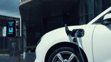 Şehir merkezinin otoparkındaki şarj istasyonuna bağlı elektrikli araba. Alternatif temiz ve sürdürülebilir enerji kullanan geleceğin yenilikçi yenilenebilir EV arabası. İnceleyin