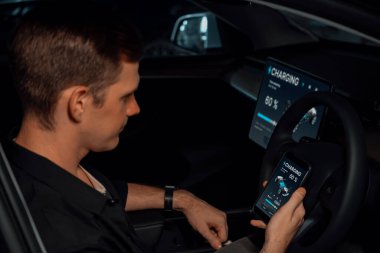Elektrikli araba sürücüsü, arabadaki uygulama ekranında şarj durumu, menzil ve şarj limitini kontrol ediyor. Akıllı teknoloji aygıtı, EV arabasının araba aküsündeki elektrik depolama verilerini şarj ettiğini gösteriyor..