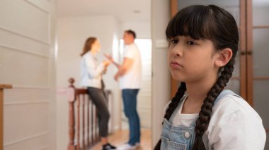 Stresli ve mutsuz genç kız arka planda ebeveynleri tartışırken köşede ağlayıp üzülüyor. Evde aile içi şiddet ve travmatik çocukluk depresyona dönüşür. Eşzamanlama