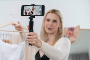 Genç sosyal medyum kadın moda videosu yapıyor. Blogcu gülümseyip telefon çubuğu selfie 'si kullanırken aynı zamanda ikna edici online giysiler izleyicilere ya da takipçilere vlog sattırıyor. Blithe