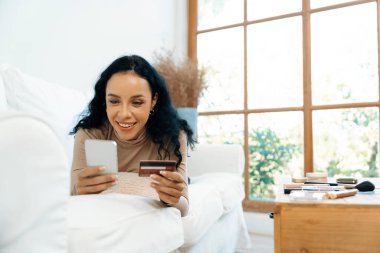 Genç mutlu bir kadın internetten alışveriş yaparak ürün satın alırken aynı zamanda internet üzerinden online kredi kartı ödeme sistemi ile çevrimiçi mağaza platformundan önemli siber güvenlik tarafından korunan ürünler sipariş ediyor.