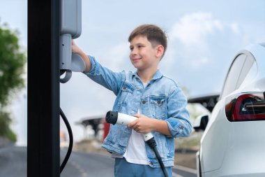 Küçük çocuk EV şarj istasyonundan çevre dostu elektrikli araba şarj ediyor. Temiz, yenilenebilir ve sürdürülebilir enerjiyle çalışan alternatif ulaşım için EV araba yolculuğu konsepti. Kalıcı