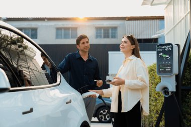 Çevre dostu aile çifti EV 'yi şarj istasyonundan şarj ediyor. EV elektrikli araba teknolojisi gelecekteki sürdürülebilirlik için alternatif ulaşım olarak kullanılıyor. Yararlı