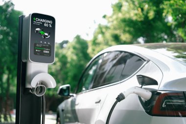 Yazın yeşil sürdürülebilir şehir bahçesinde elektrikli araba şarj oluyor. Kentsel sürdürülebilirlik yaşam tarzı yeşil temiz yeniden şarj edilebilir enerji elektrikli BEV araç iç organları