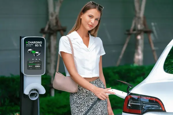 Genç bir kadın yazın yeşil sürdürülebilir şehir bahçesinde EV elektrikli arabasıyla seyahat ediyor. Kentsel sürdürülebilirlik yaşam tarzı yeşil temiz yeniden şarj edilebilir enerji elektrikli BEV araç iç organları