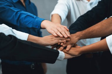 Çeşitli ofis çalışanlarından oluşan bir grup, ofis odasında el ele vererek iş sinerjisini ve iş yerindeki güçlü verimli takım çalışmasını sembolize ediyor. İş çalışanları arasındaki işbirliği ve birlik. Tedbirli
