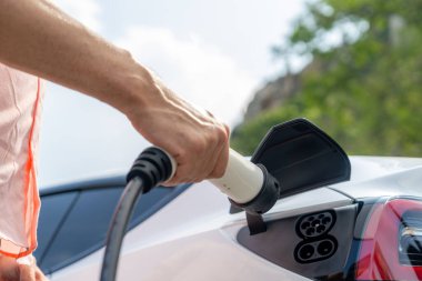Dışarıdaki şarj istasyonundan EV şarj aletini şarj etmek için elektrikli araca elle tak. Alternatif temiz ve sürdürülebilir enerji kavramına sahip taze gün ışığı ortamı. Kalıcı