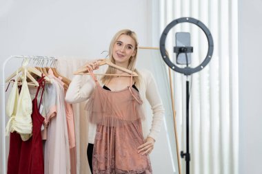 Genç sosyal medyum kadın moda videosu yapıyor. Blogcu kameraya ve ışık çemberine gülümserken, aynı zamanda ikna edici çevrimiçi kıyafetleri izleyicilere veya takipçilere vlog sattırıyor. Blithe