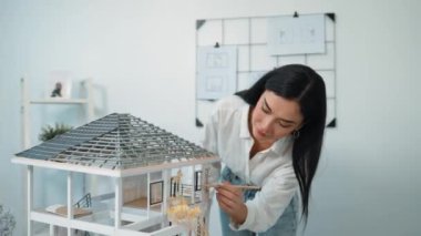 Genç, güzel ve zeki mühendisin yakın çekimleri modern ofiste duvarında taslak olan kalem kullanarak ev modelini ölçmeye odaklanıyor. Yaratıcı yaşam ve tasarım konsepti. Tertemiz..