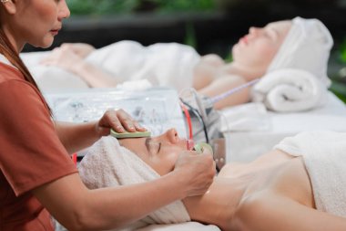 Güzel genç kadınlar profesyonel doktordan yüz masajı alırken spa yatağında yatarlar. Cildi elektrikli yüz makinesiyle çevrili çekici bir kadın. Huzur.