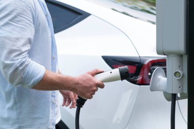 Yakından el yerleştirme ve şarj etmek için EV şarj cihazı şarj istasyonundan şarj ediliyor. Alternatif enerji, gelecekteki sürdürülebilirlik için çevre dostu taşımacılığında kullanılıyor. Eşzamanlama