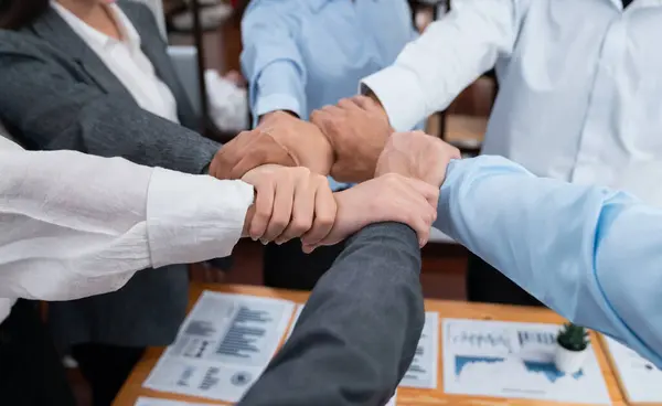 Diverse team of officer workers hold hands in circle, showing solidarity and teamwork in corporate office. Businesspeople form strong community built on integrity and collaboration. Concord