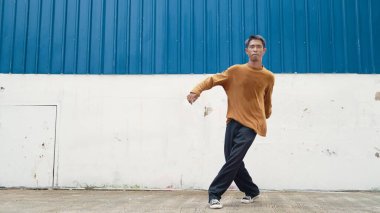 İspanyol adam kollarını açıp duvarın önünde dans ediyor. Modern dansçı ya da koreografın, günlük kıyafetleriyle hip hop stiliyle dans ederken ki hareketli çekimi. Açık hava sporu 2024. ÇalışmaComment.