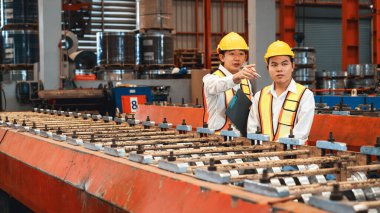 Ağır sanayi fabrikasındaki çelik üretim hattında endüstriyel malların optimal kalitede üretimi için mühendis tarafından denetlenirken fabrika işçisi metal damgalama makinesini çalıştırıyor. Örnek gösteriliyor