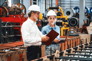 Metal imalatında makine mühendisliği denetleyicisi olarak liderlik örneğini sunan çelik endüstriyel makineyi incelemek için dizüstü bilgisayar kullanan fabrika mühendisi ve asistan..