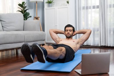 Atletik ve sporcu adam spor paspası üzerinde çatırdarken evdeki formda fiziğe ve sağlıklı spor yaşam tarzına uygun online ev eğitimi takip ediyor. Çevrimiçi neşeli ev egzersizi videosu.
