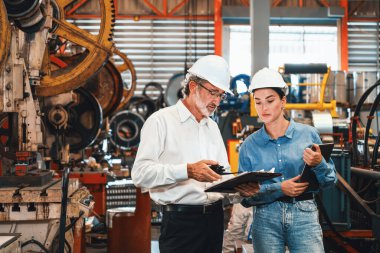 Metal imalatında makine mühendisliği denetleyicisi olarak liderlik örneğini sunan çelik endüstriyel makineyi incelemek için dizüstü bilgisayar kullanan fabrika mühendisi ve asistan..