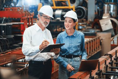 Metal imalatında makine mühendisliği denetleyicisi olarak liderlik örneğini sunan çelik endüstriyel makineyi incelemek için dizüstü bilgisayar kullanan fabrika mühendisi ve asistan..