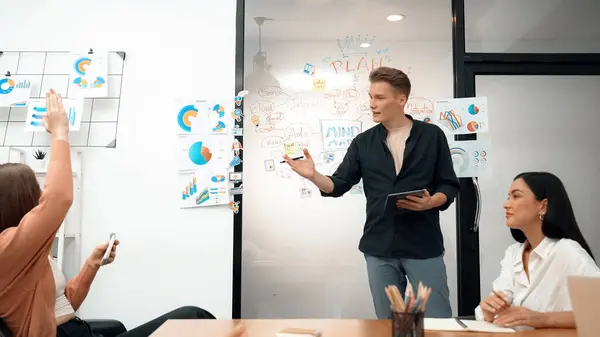 Professional male leader presents start up project by using mind map, colorful sticky notes and business statistic graph with confident while investor raising hand and asking question. Immaculate.