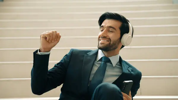 Closeup of smart business man listening and enjoy music while wear headphone. Project manager smiling while getting good news, getting promotion, increasing sales. Relaxing man enjoy music. Exultant.