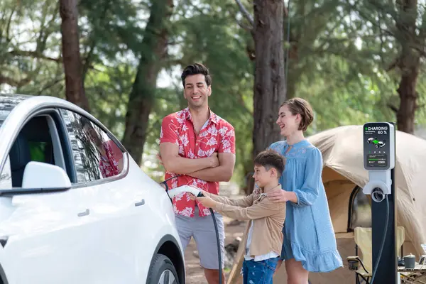 stock image Outdoor adventure and family vacation camping in nature travel by eco friendly car for sustainable future. Lovely family recharge EV car with EV charging station in campsite. Perpetual