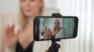 Genç sosyal medyum kadın selfie çubuğuyla moda videosu yapıyor. Blogcu kameraya gülümserken çevrimiçi kıyafetleri izleyicilere ya da takipçilere vlog sattırıyor. Blithe