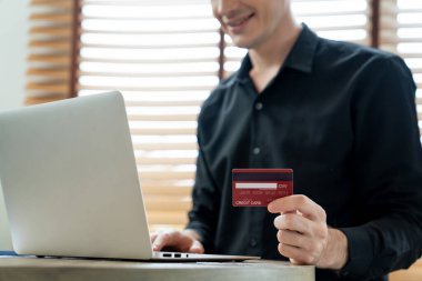 Genç adam internet bankacılığı için kredi kartlı dizüstü bilgisayar kullanıyor. İnternet üzerinden alışveriş yapıyor. Banka kartıyla modern ve kullanışlı online satın alma. Açılıyor