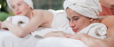 Beyaz havluyla beyaz bir spa yatağında dinlenen ve profesyonel bir masaj salonundaki masörle vücut masajı yapan birkaç güzel beyaz kadının portresi. Huzur..