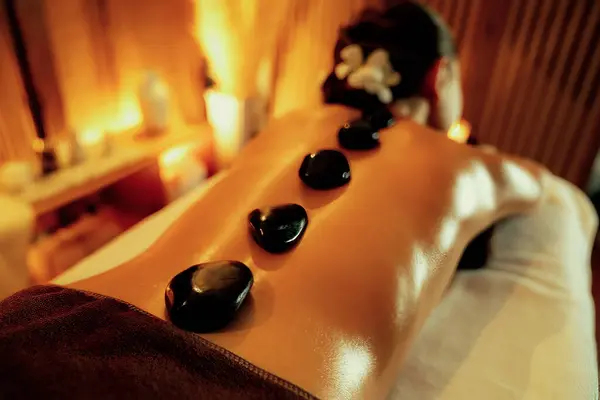 温泉浴场的热石材按摩在豪华度假胜地与温暖的烛光 快乐的女性顾客享受温泉浴池的玄武岩按摩滑翔身体与舒缓的温暖 — 图库照片