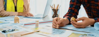 Profesyonel mimar ve mühendis, planlı, ahşap bloklu ve ağaç modelli bir toplantı masasında çevre dostu ev tasarlamak için işbirliği yapıyorlar. - Yakın çekim. Tanımlama.