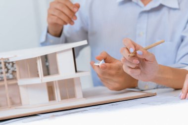 Profesyonel erkek mühendis ev modelini cetvel kullanarak ölçerken güzel bir iş arkadaşı da plan üzerinde yazarak birlikte çalışıyor. Yaratıcı tasarım ve takım çalışması. - Yakın çekim. Tertemiz..