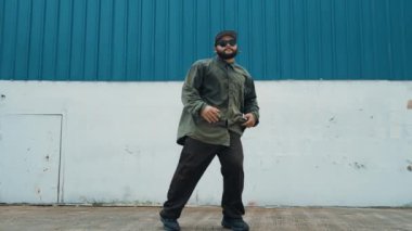 Sokak ortasında mavi duvarlı hippi dansçı ayak basamağı. Asyalı break dansçı kollarını açarken sokak dansı yapıyor. Hip hop koreografı enerjik bir dans sergiliyor. Açık hava sporu 2024 hiphop..