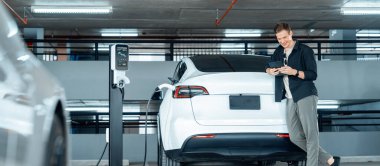 Genç adam EV elektrikli arabasıyla alışveriş merkezinin otoparkına gidiyor şehir merkezindeki şarj oluyor yeşil, temiz, yeniden şarj edilebilir elektrikli araç iç organları ile kentsel sürdürülebilirlik yaşam tarzını gösteriyor