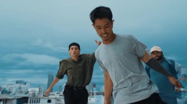 Bir grup çok kültürlü hippi çatıda işaret fişeği çalıyor. Zenci dumanı tutan çekici bir sokak dansçısı hip-hop müzik eşliğinde break dans yapıyor. Açık hava sporu 2024. Sokak dansı. hiphop.