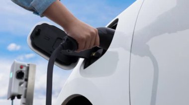 Asyalı adam şarj istasyonundan elektrikli arabaya akıllı EV şarj aleti takıyor. EV araba konseptiyle sürdürülebilir ve temiz ulaşım teknolojisi için gelecekteki alternatif enerji kullanımı. İnceleyin