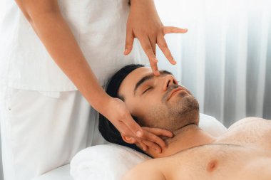 Beyaz adam stres önleyici kafa masajından ve lüks bir tatil beldesi veya otel spa salonundaki modern ışık ortamında yüz güzelliği eğlencelerini şımartmaktan hoşlanıyor. Sessiz.