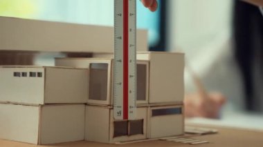 Cetvel ölçü evi modelini kullanan yetenekli profesyonel mühendis elini kapatırken, genç yetenekli mimar da taslak çiziyor. Yaratıcı ve profesyonel tasarım. Eline odaklan. Tertemiz..