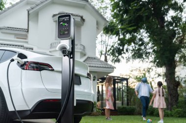 Evde şarj edilen elektrikli araba şarjını mutlu ve neşeli bir ailenin arka planına odakla. EV arabası daha iyi bir gelecek için alternatif ve sürdürülebilir enerji kullanıyor.