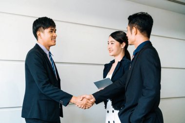 İş adamları konsepti kabul ediyor. İş adamı toplantı odasında başka bir iş adamıyla tokalaşıyor. Genç Asyalı sekreter bayan onların yanında duruyor. uds