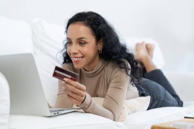 Genç mutlu bir kadın internetten alışveriş yaparak ürün satın alırken aynı zamanda internet üzerinden online kredi kartı ödeme sistemi ile çevrimiçi mağaza platformundan önemli siber güvenlik tarafından korunan ürünler sipariş ediyor.