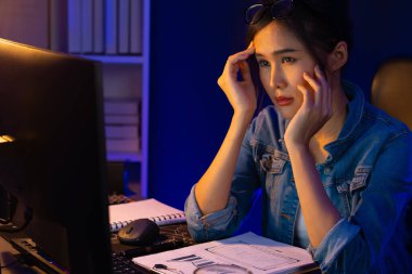 Stresli, genç, güzel Asyalı yaratıcı proje yaratıcısı sosyal medyayı araştırmak için bilgisayara bakıyor ve geceleri daha çok neon modern ofisin planlama kanalı stratejisine ulaşılıyor. Taktik.