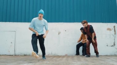 Genç sokak dansçısı hip hop tarzında dans ediyor ve çok kültürlü arkadaşları duvarın arkasında tezahürat yapıyor. Çekici yakışıklı adam mavi arka planda kollarını uzatıyor. Açık hava sporu 2024 hiphop..