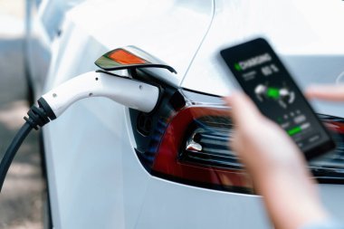 EV 'yi şarj etmek için elektrikli araca EV şarj prizi tak, akıllı telefon EV uygulamasında pil durumu görüntüsü. Ulaşım için alternatif temiz ve sürdürülebilir enerji. Kalıcı
