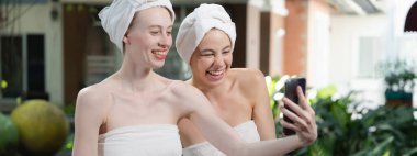 Beyaz havluyla güzel ciltli bir çift güzel kadın açık havada barışçıl doğal çevreyle çevrili bir şekilde fotoğraf çekiyorlar. Güzellik ve sağlıklı spa konsepti. Huzur.