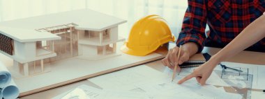 Kooperatif mimar ekibinin kesilmiş görüntüsü ev modeli, güvenlik miğferi ve mimari planlarla toplantı masasında birlikte çalışmaya karar verir ve birlikte çalışırlar. - Yakın çekim. Eline odaklan. Filizlenen.