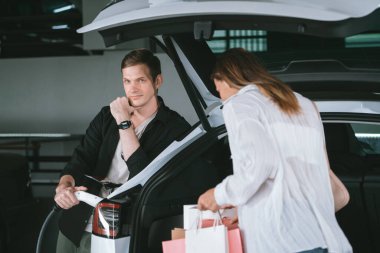 Genç bir kadın EV elektrikli arabasıyla alışveriş merkezinin otoparkına gidiyor şehir merkezinde elektrik iç organlarının yeşil temiz şarj edilebilir enerji ile sürdürülebilirlik yaşam tarzını gösteriyor.