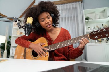 Genç Afrikalı Amerikalı müzisyenin sunucu kanalı gitar çalıyor, şarkı söylüyor, stüdyoda dizüstü bilgisayardan yayın yapıyor. Kulaklık dekorasyonu ve mikrofon kaydı. Tatlandırıcı.