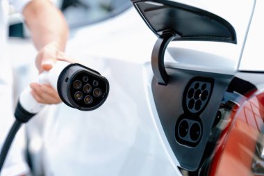 Dışarıdaki şarj istasyonundan EV şarj aletini şarj etmek için elektrikli araca elle tak. Alternatif temiz ve sürdürülebilir enerji kavramına sahip taze gün ışığı ortamı. Kalıcı